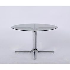 a round glass table with chrome legs on a white background in front of a plain backdrop