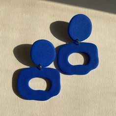 two blue earrings sitting on top of a white cloth covered floor next to each other