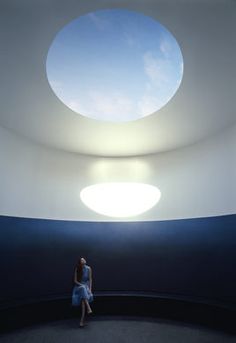 a woman is sitting in the middle of a room with a skylight above her