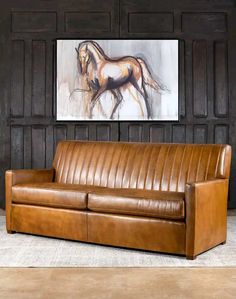 a brown leather couch sitting in front of a painting