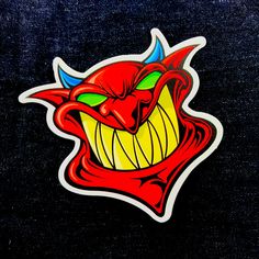 an angry red demon sticker on a black background with yellow teeth and fangs in the mouth