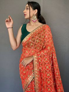 Look stunning in this classic orange printed georgette festival wear saree with a blouse! The saree is 5.50 meters long and made of high-quality georgette material with bandhani print all over, and gotta pati lace border with tassels work. The green blouse in georgette material with a gotta patti lace border adds a beautiful contrast to the saree. The saree is perfect for weddings, festivals, events, or even casual wear. It's customizable and comes with an stitched 1.00 meters blouse. Festive Saree, Georgette Material, Bandhani Print, Kids Party Wear Dresses, Kids Party Wear, Pretty Orange, Gotta Patti, Color Plain, Print Saree