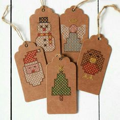 four tags with christmas designs on them hanging from twine strings, one has a small tree and the other has an ornament