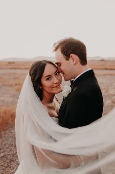 a bride and groom are standing in the desert with their veil blowing in the wind