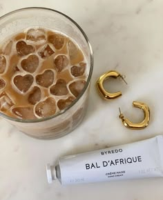 a glass with liquid and gold earrings next to a tube of bal d'afrique