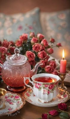 a tea set with pink roses and a lit candle next to it on a table