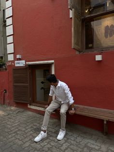 a man sitting on a wooden bench in front of a red building with shutters