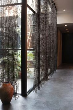 a vase sitting on the floor in front of a window covered with metal mesh curtains