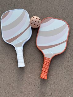 two ping pong paddles laying next to each other on the ground with a ball