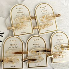 four gold and white business cards with writing on them, one has a pen in it