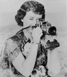 an old photo of a woman holding a camera and looking through the lens to take pictures