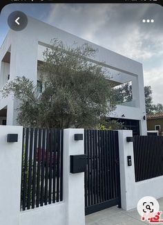 a white house with a black gate and trees in front of it on a cloudy day