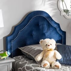 a white teddy bear sitting on top of a blue headboard in a bed room