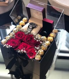 a box with roses and chocolates in it on a table next to a watch