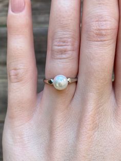 a woman's hand with a ring on it that has a white pearl in the middle