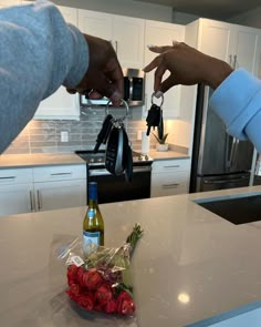 two people holding keys and handing them to each other on a kitchen counter with flowers in the foreground