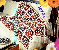 a white couch covered in a colorful crochet afghan next to flowers and plates