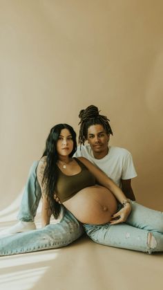 a pregnant woman sitting on the floor next to a man who is holding her belly