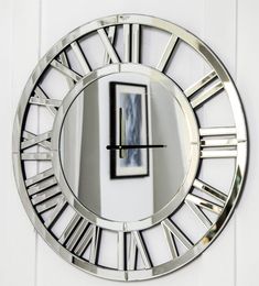 a large round mirror with roman numerals on the face is shown in front of a white wall