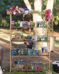 an outdoor bar cart filled with glasses and vases on top of grass next to a tree