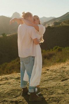 a man and woman standing on top of a hill with their arms around each other