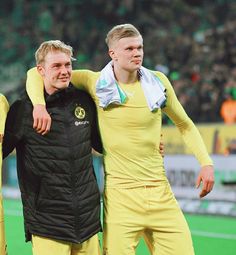 two men in yellow uniforms standing next to each other on a soccer field with fans in the background