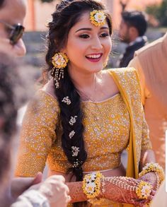 a woman with long hair wearing a yellow outfit and holding flowers in her hair, smiling at the camera