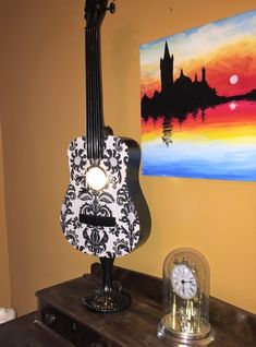 an acoustic guitar sitting on top of a wooden table next to a clock and painting