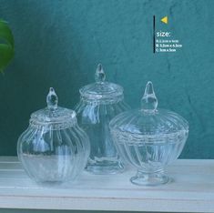 three clear glass jars sitting on top of a white shelf next to a green plant