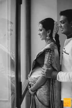 a man and woman standing next to each other near a glass window in black and white