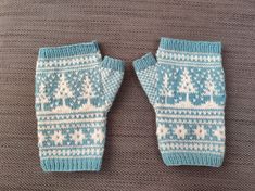 two knitted mittens sitting on top of a bed covered in blue and white snowflakes