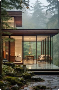 a modern house in the woods surrounded by rocks and trees, with large glass walls