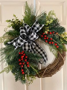 a christmas wreath hanging on a door with red berries and greenery tied to it