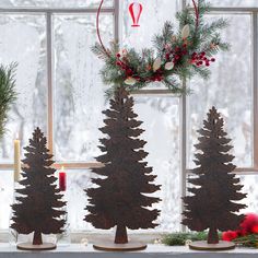 three wooden christmas trees sitting on top of a window sill next to a candle