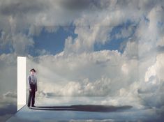 a man standing in the middle of a doorway with clouds behind him and his shadow on the ground