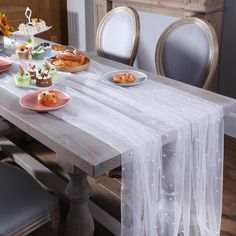 the table is set with desserts and pastries on it, along with two chairs