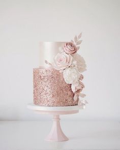 a pink and gold wedding cake with flowers on the top is sitting on a white pedestal