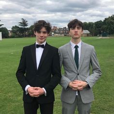 two young men in suits standing next to each other on a grass covered field with houses in the background