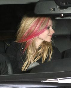 a woman with pink hair sitting in a car looking out the window at someone else