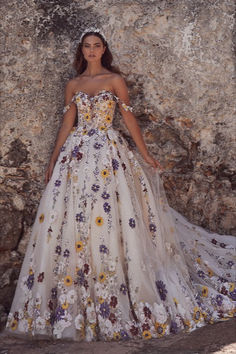 a woman standing in front of a stone wall wearing a dress with flowers on it