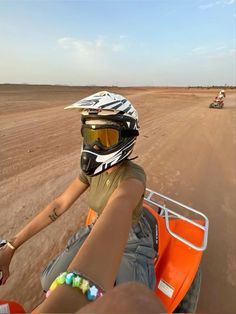 a person riding on the back of an orange motorcycle down a dirt road next to a field