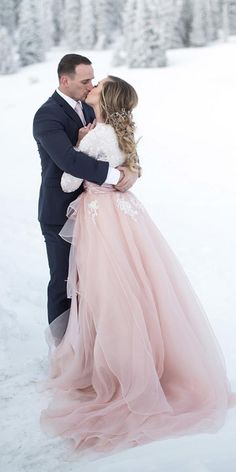 a bride and groom kissing in the snow with trees in the background