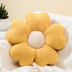 a yellow knitted flower sitting on top of a bed next to a potted plant