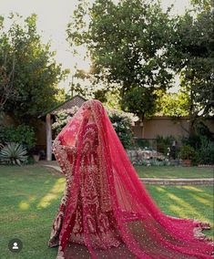 the back of a woman's head in a red dress and veil on grass