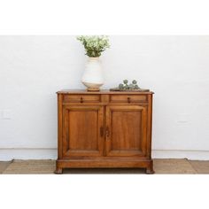 a vase with flowers sitting on top of a wooden cabinet next to a white wall