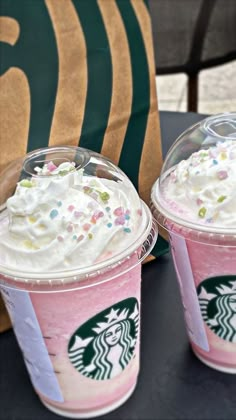 two starbucks drinks with whipped cream and sprinkles sitting on top of a table