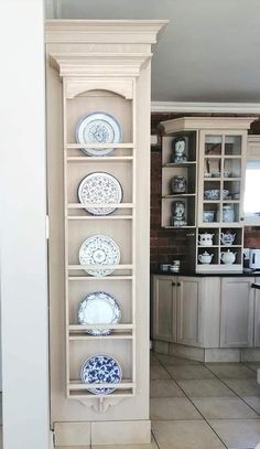 a tall shelf filled with plates on top of a tiled floor next to a kitchen