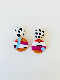 two pairs of colorful earrings on a white surface, one has a blue arrow and the other has an orange circle