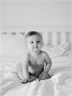 a black and white photo of a baby sitting on a bed looking at the camera