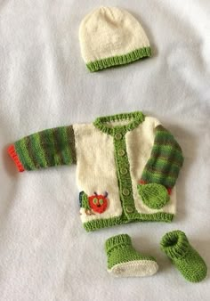 a knitted green and white sweater, booties and hat are laying on a bed